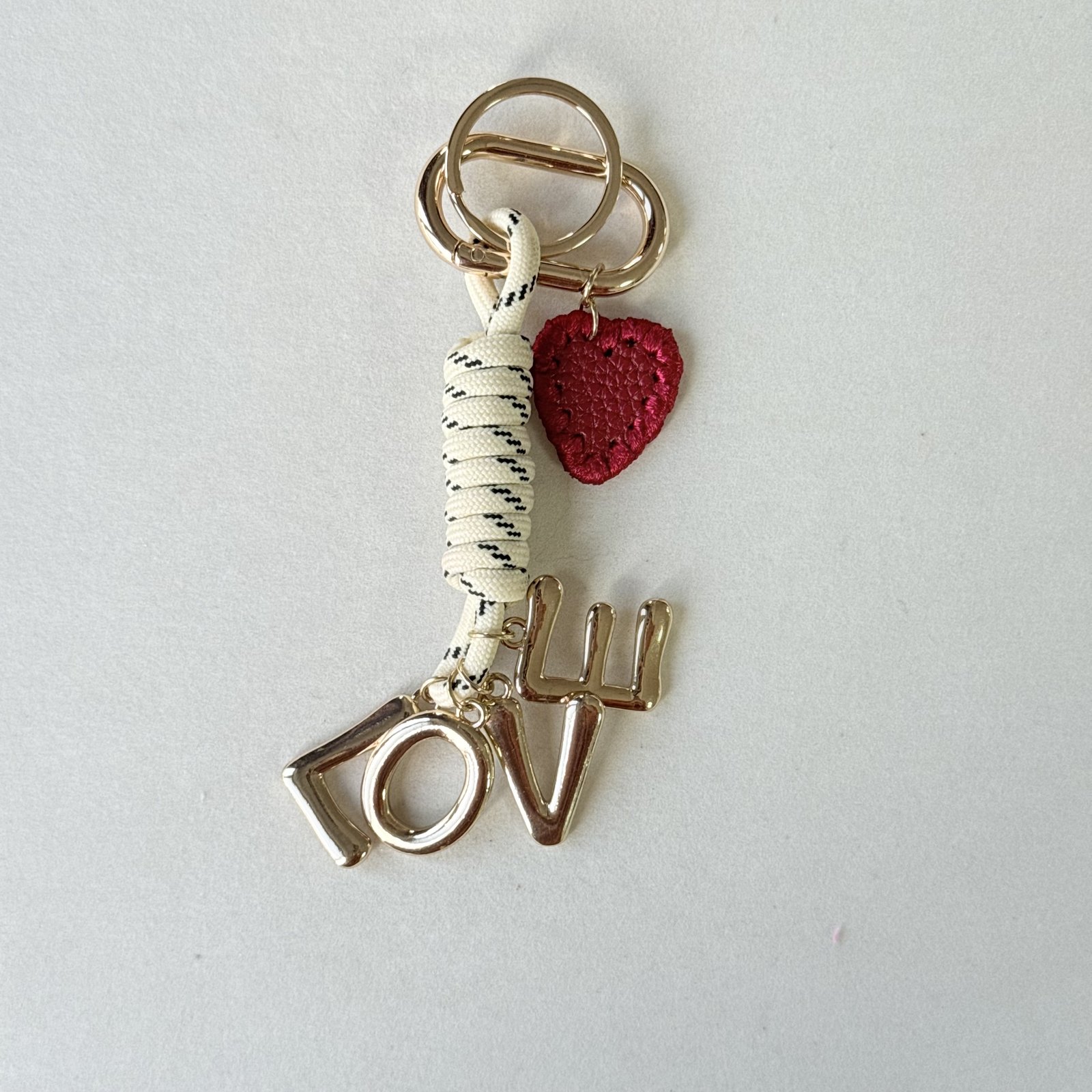 LOVE and textured heart charms with wrapped cord in gold-tone, red, cream, black, shown as a keychain.