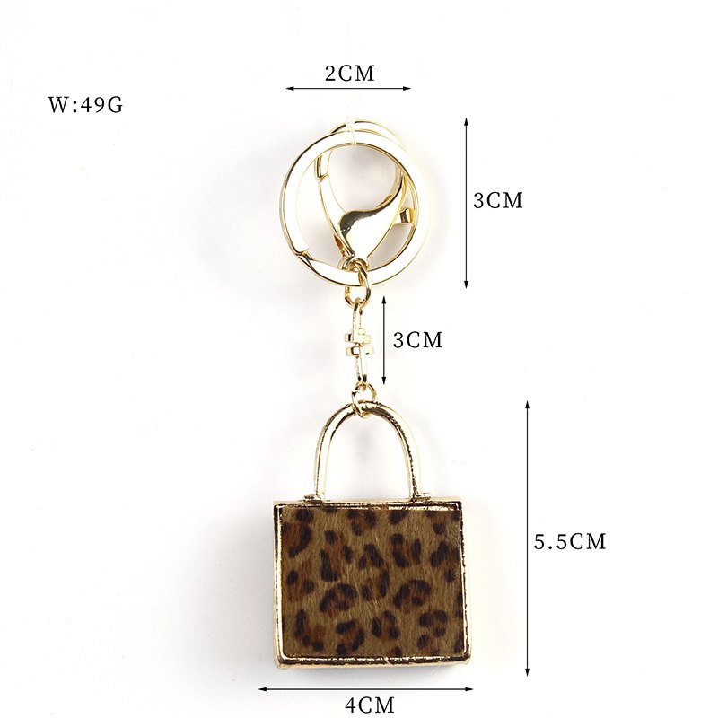 Rectangular handbag-shaped pendant with animal print, arched handle, ring and clip in brown, black, gold-tone, shown as a keychain.