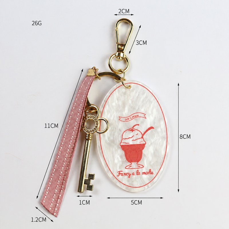 Oval printed drink pendant with lettering, long strap, key-shaped charm, ring and clip in white, red, pink, gold-tone, shown as a keychain.