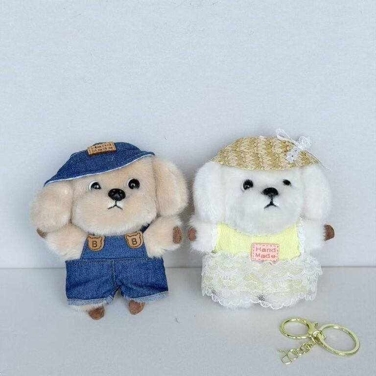 Two plush dog charms, one in blue overalls and one in a white dress, with small hats