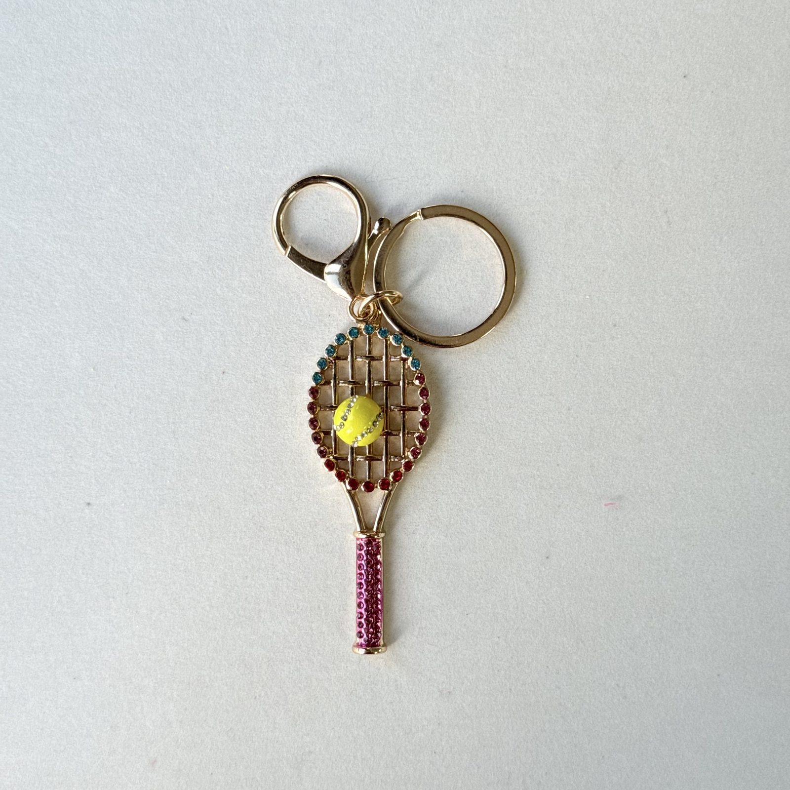 Tennis-racket and ball charm in brown, burgundy, yellow, gold-tone, shown as a keychain.