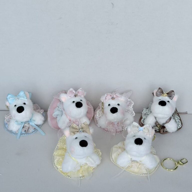 White plush dog charms wearing pastel dresses and bows, arranged on a shelf
