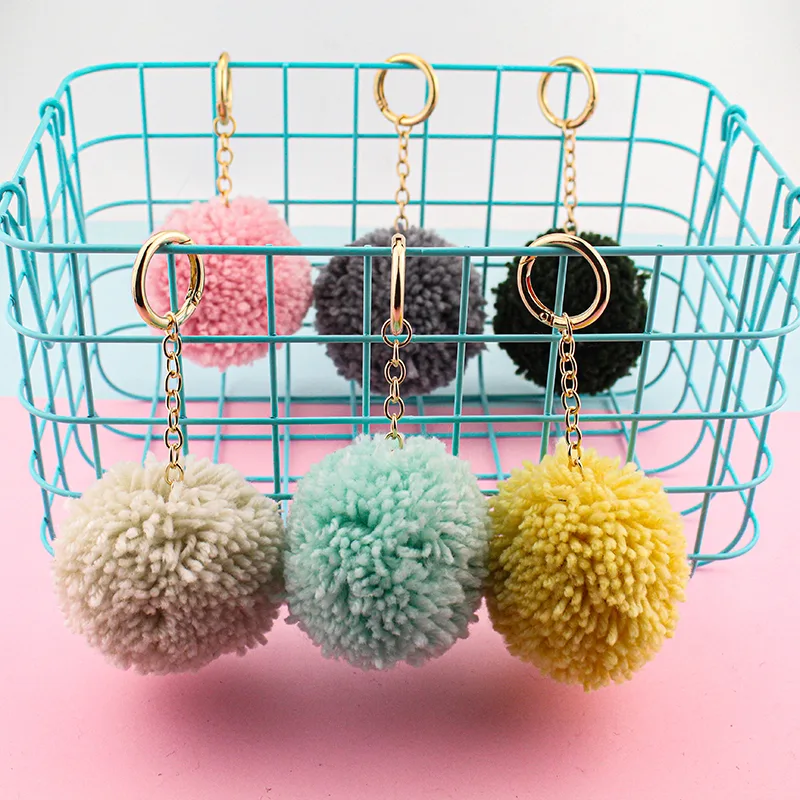 Six pom-pom charms in different colours, each attached to a short chain and ring on a wire basket.