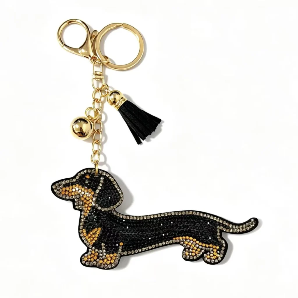 Stone-covered long-body dog charm with ball and tassel and ring and clasp in black, tan, gold-tone, shown as a keychain.