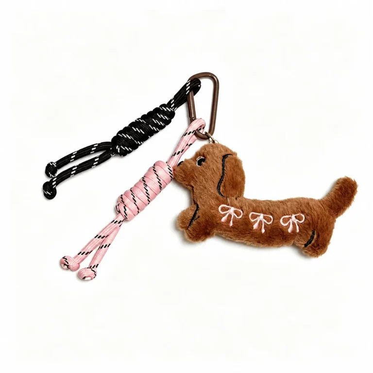 Fuzzy dachshund with bow stitching and cord tassels and clasp in brown, pink, black, white, shown as a clip-on charm.