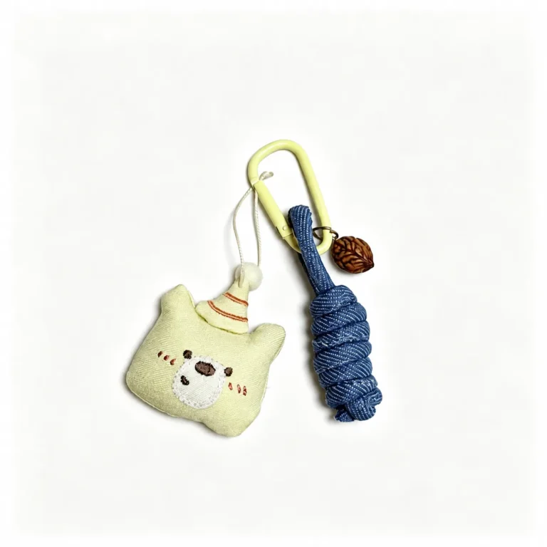 Fuzzy bear face with party hat and cord tassels and clasp in cream, blue, brown, shown as a clip-on charm.