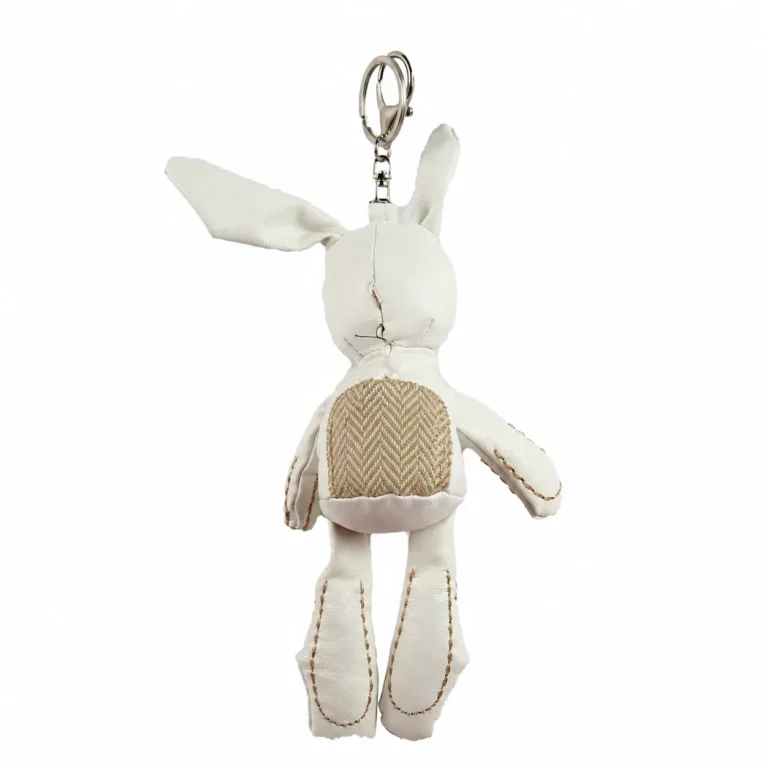 Reverse of rabbit-shaped padded figure with small backpack, chain and clip in cream, brown, silver-tone, shown as a keychain.