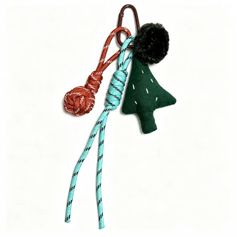 Flat tree charm with pom-pom and knotted cord tassels and clasp in green, black, turquoise, red, silver-tone, shown as a clip-on charm.