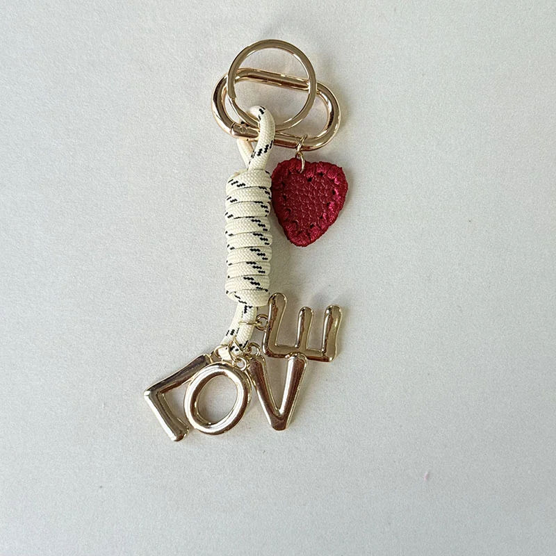 Gold-tone LOVE letters, a red heart and wrapped cream cord on a ring clasp