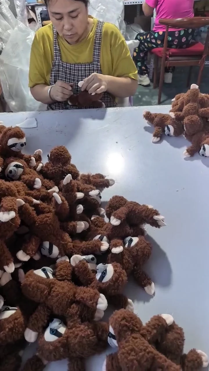Video frame of an operator hand finishing a small brown plush piece beside similar pieces