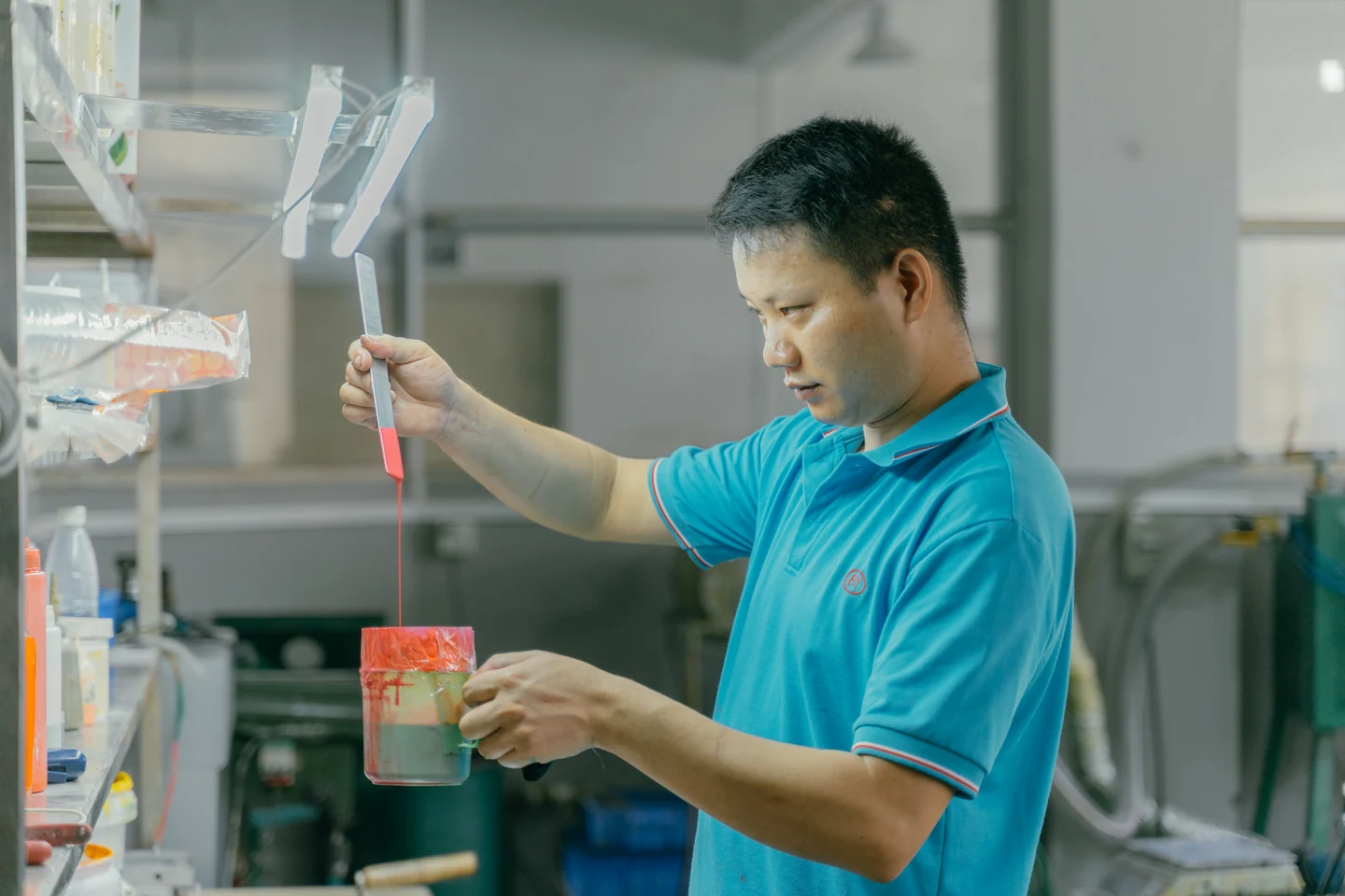 Operator lifting red material with a metal tool above a container
