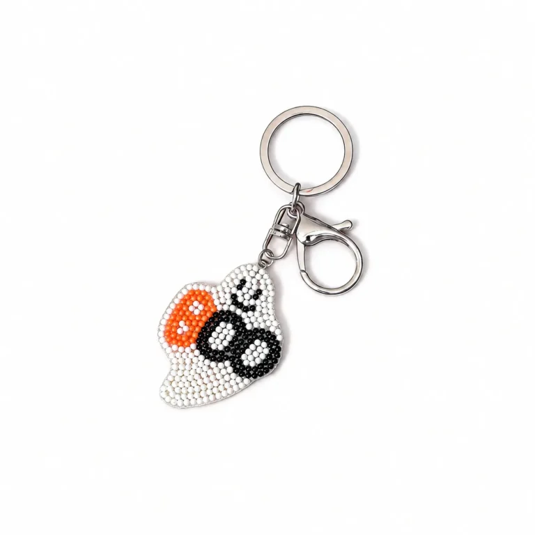 Beaded ghost charm with pumpkin accent and clasp and round ring in white, black, orange, silver-tone, shown as a keychain.