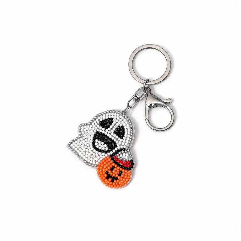 Beaded ghost-face charm with pumpkin accent and clasp and round ring in white, black, orange, silver-tone, shown as a keychain.