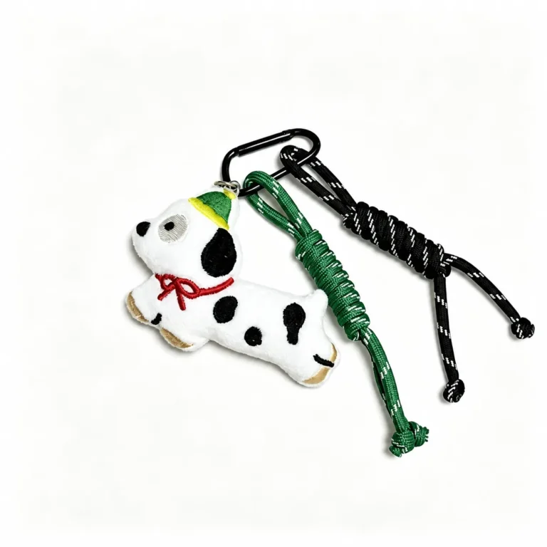 Fuzzy spotted dachshund with bow and cord tassels and clasp in white, black, red, green, shown as a clip-on charm.